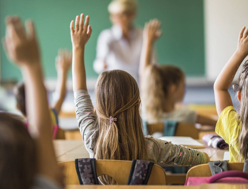 Students raise their hands in a full classroom