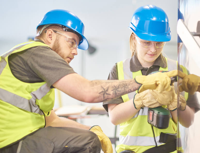 Two people wearing high-vis vests perform a construction task