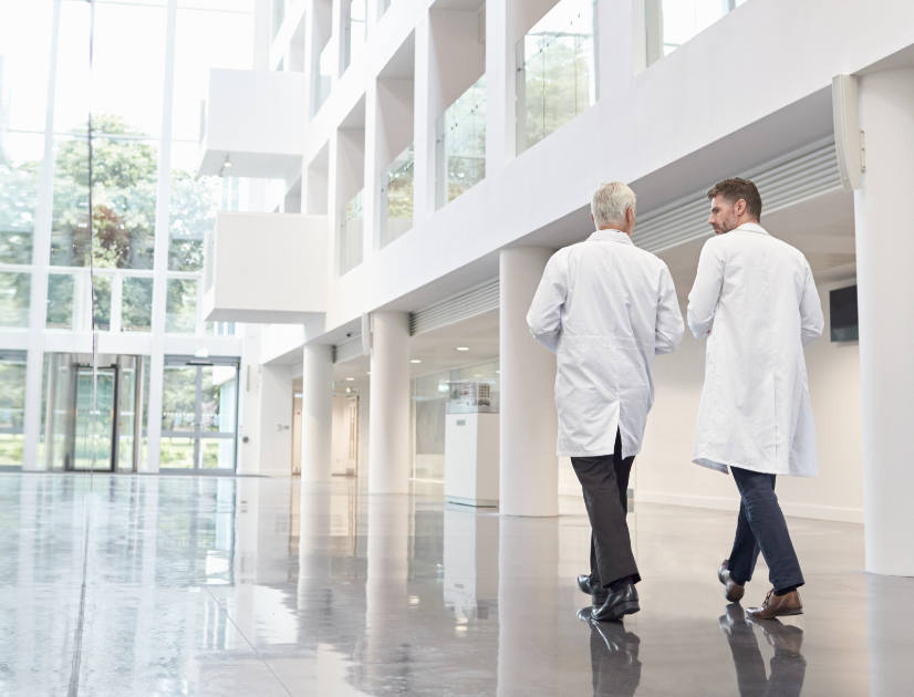 Two people wearing lab coats walk through an airy lobby foyer