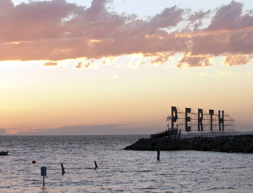 Silhouette of a cutout sign that says Perth on the shore at sunset