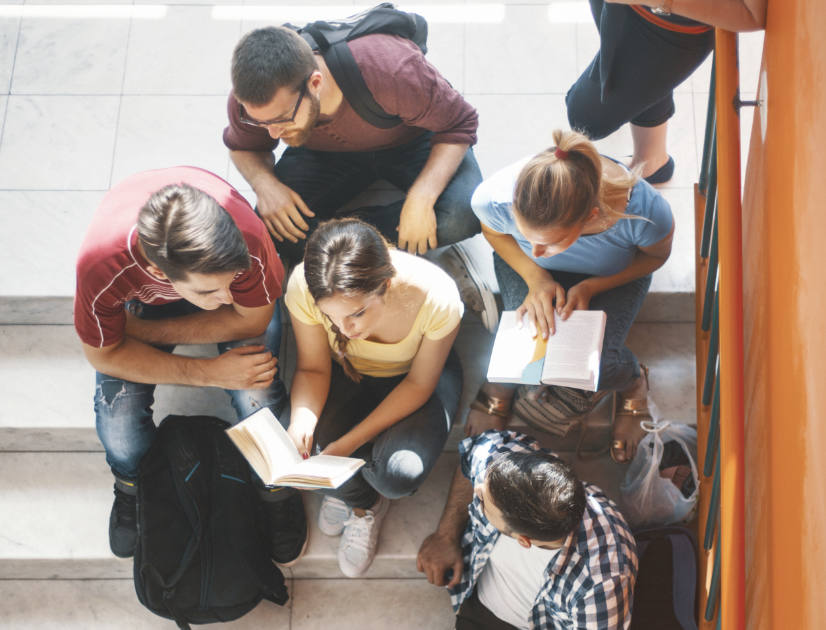 A group of students sit in a stairwell, reading a book together